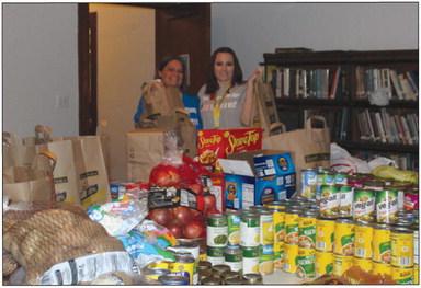 Theresa Coker and Marjeyn Schindlback gather up donated items, preparing to fill baskets for the American Legion’s family food basket give-a -away.