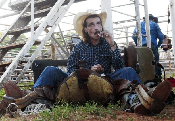 Parker Cassidy, from Bristow, cops a smoke while adjusting his saddle prior to the ranch bronc riding at the Chandler Open Rodeo. Brian Blansett photo Tri-County Herald
